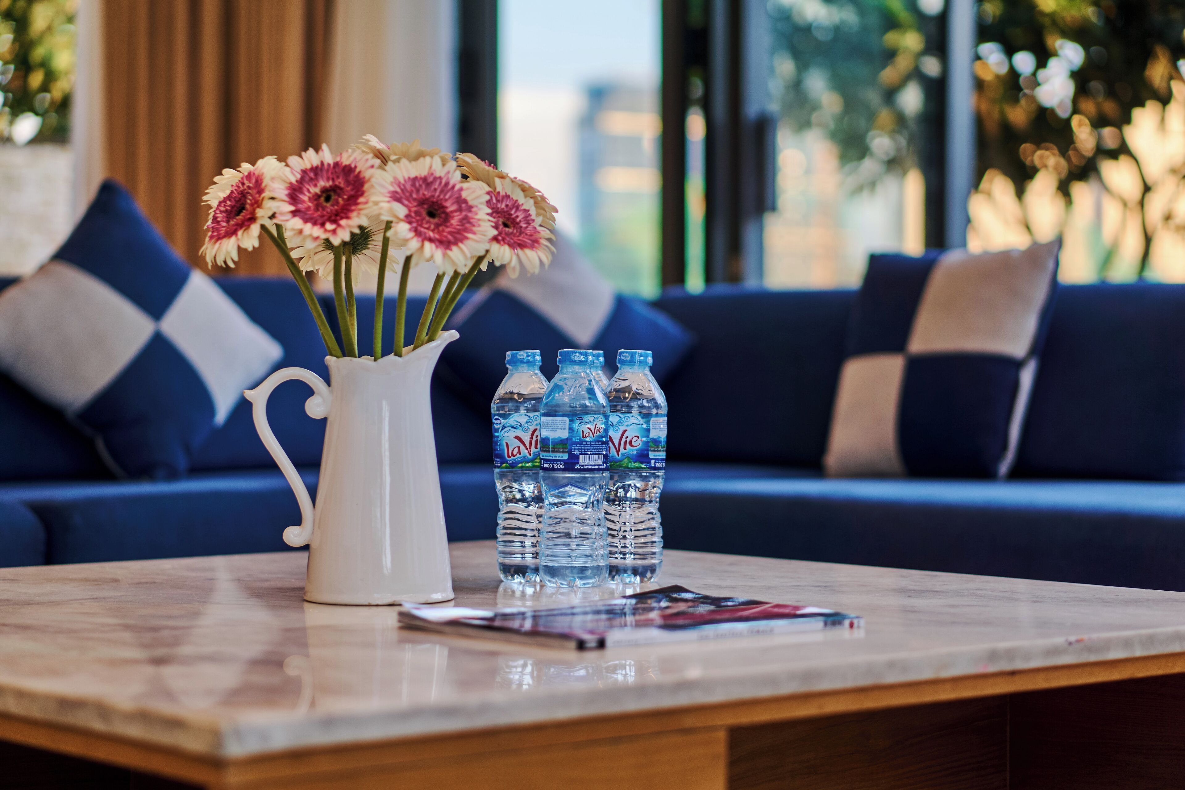 A table with a vase of flowers, water bottles, and a magazine.