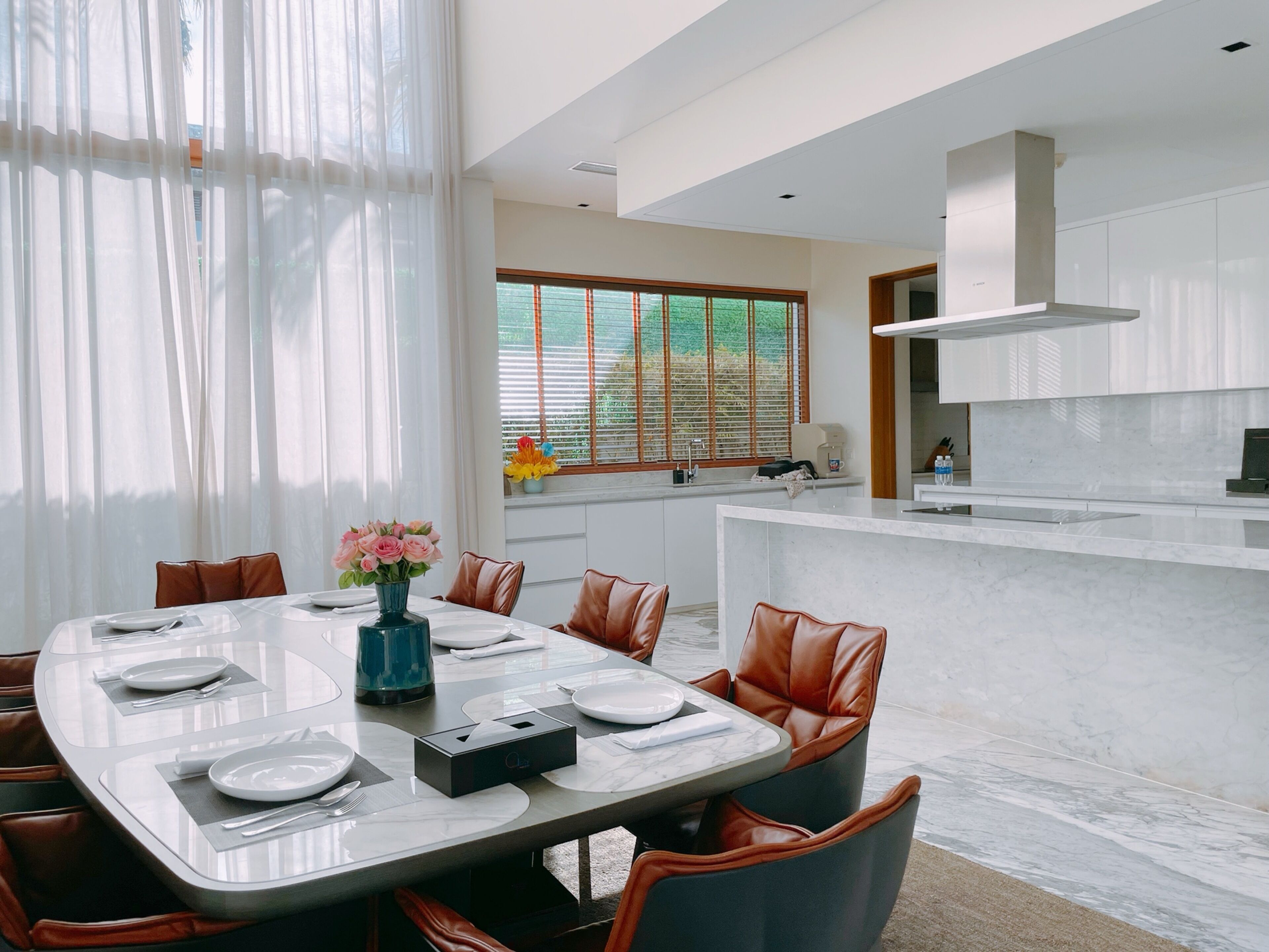A modern dining area with a marble table, leather chairs, and a vase of flowers.