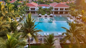 A resort with multiple swimming pools, palm trees, and buildings with red roofs. - The Ocean Suites (Da Nang)