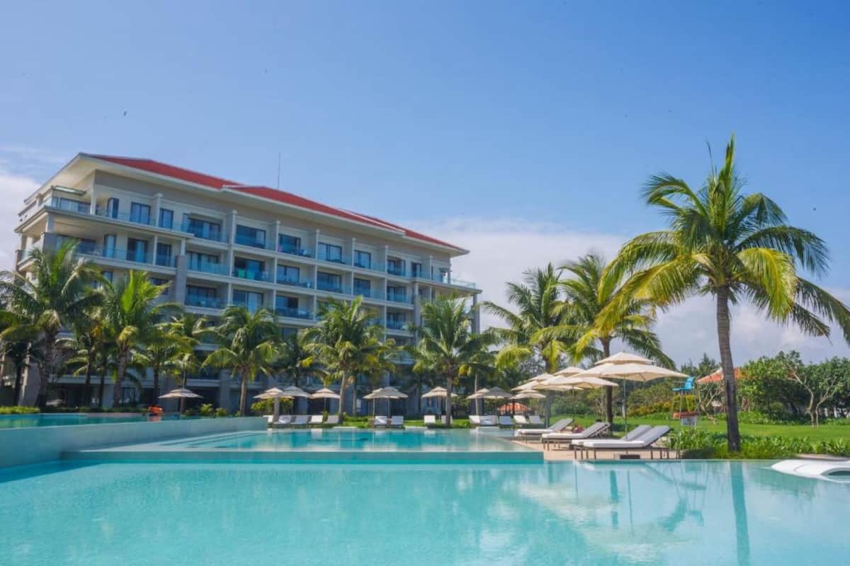 A hotel with a swimming pool, palm trees, and lounge chairs.