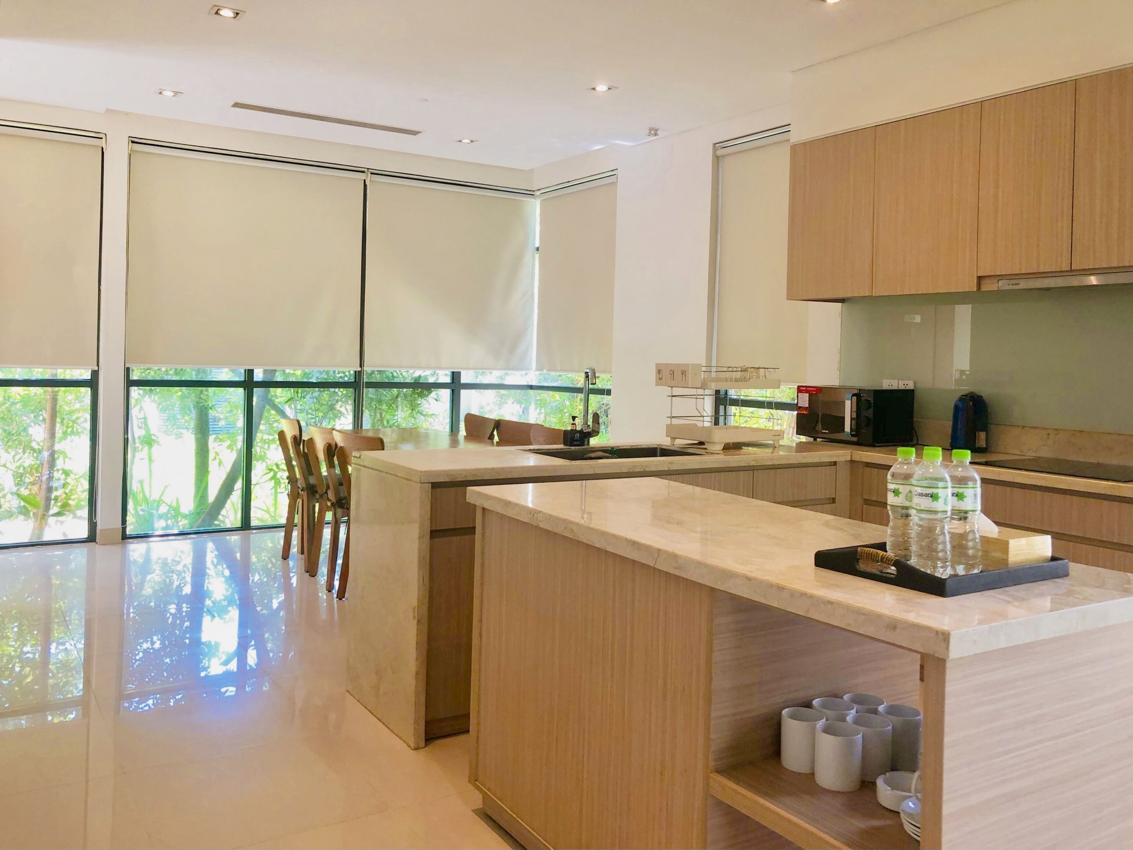 A modern kitchen with wooden cabinets, a central island, and a view of greenery outside.