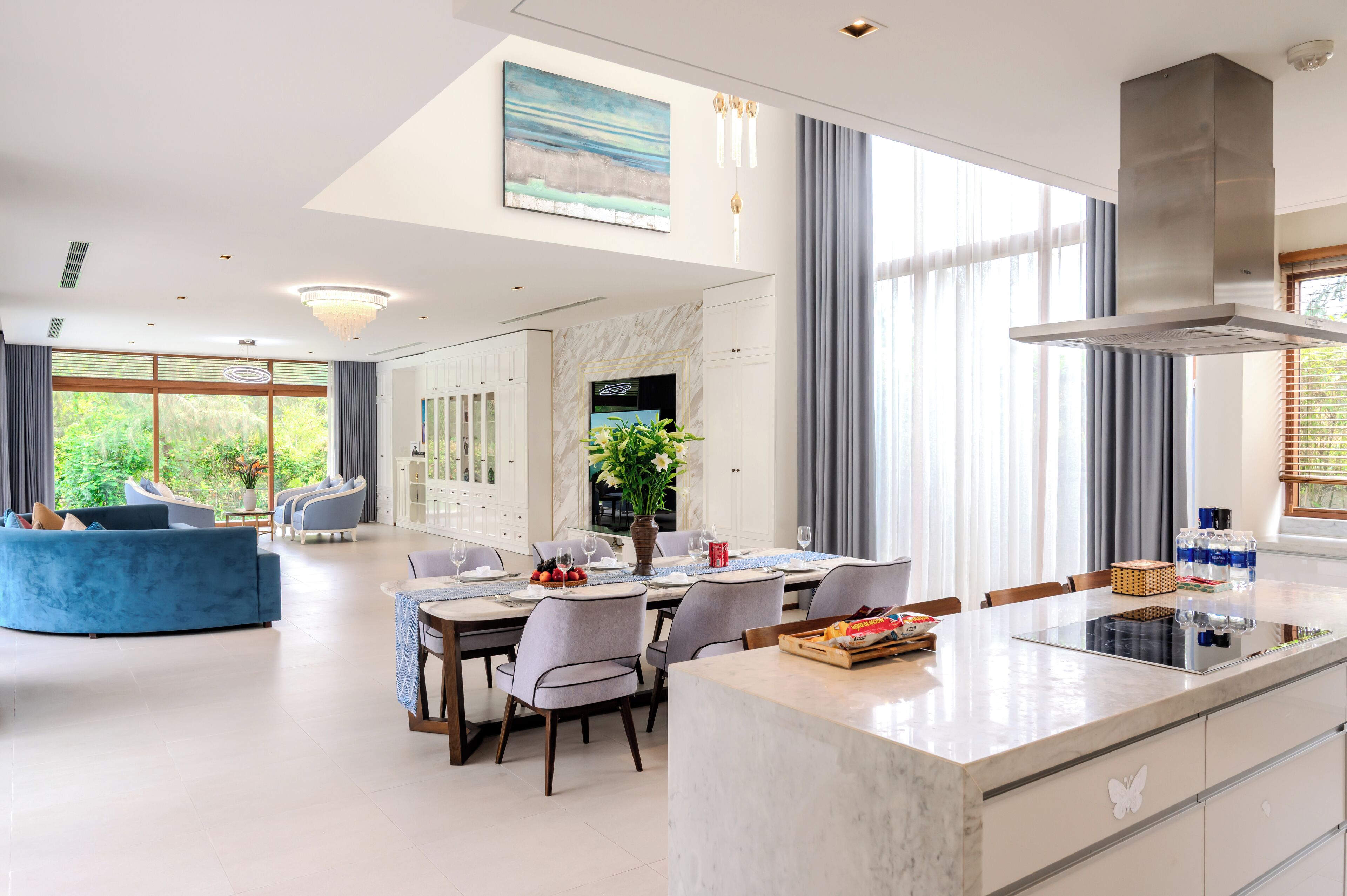 Cozinha moderna com ilha central, área de refeições com cadeiras e uma grande janela com cortinas.