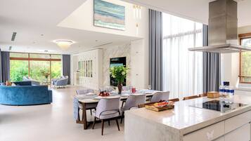 Cozinha moderna com ilha central, área de refeições com cadeiras e uma grande janela com cortinas.