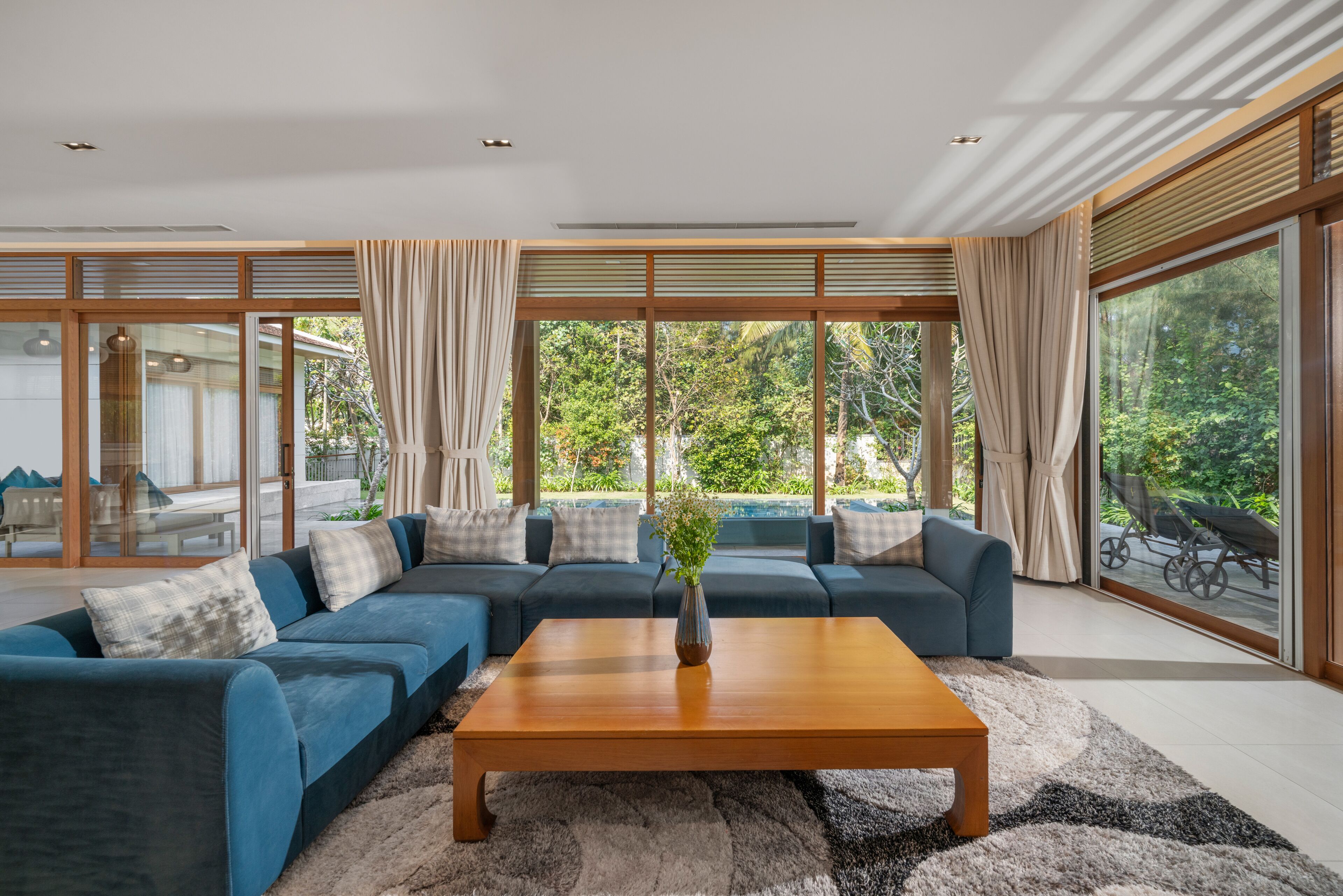 Een moderne woonkamer met een modulaire bank, een houten salontafel en grote ramen met uitzicht op groen.