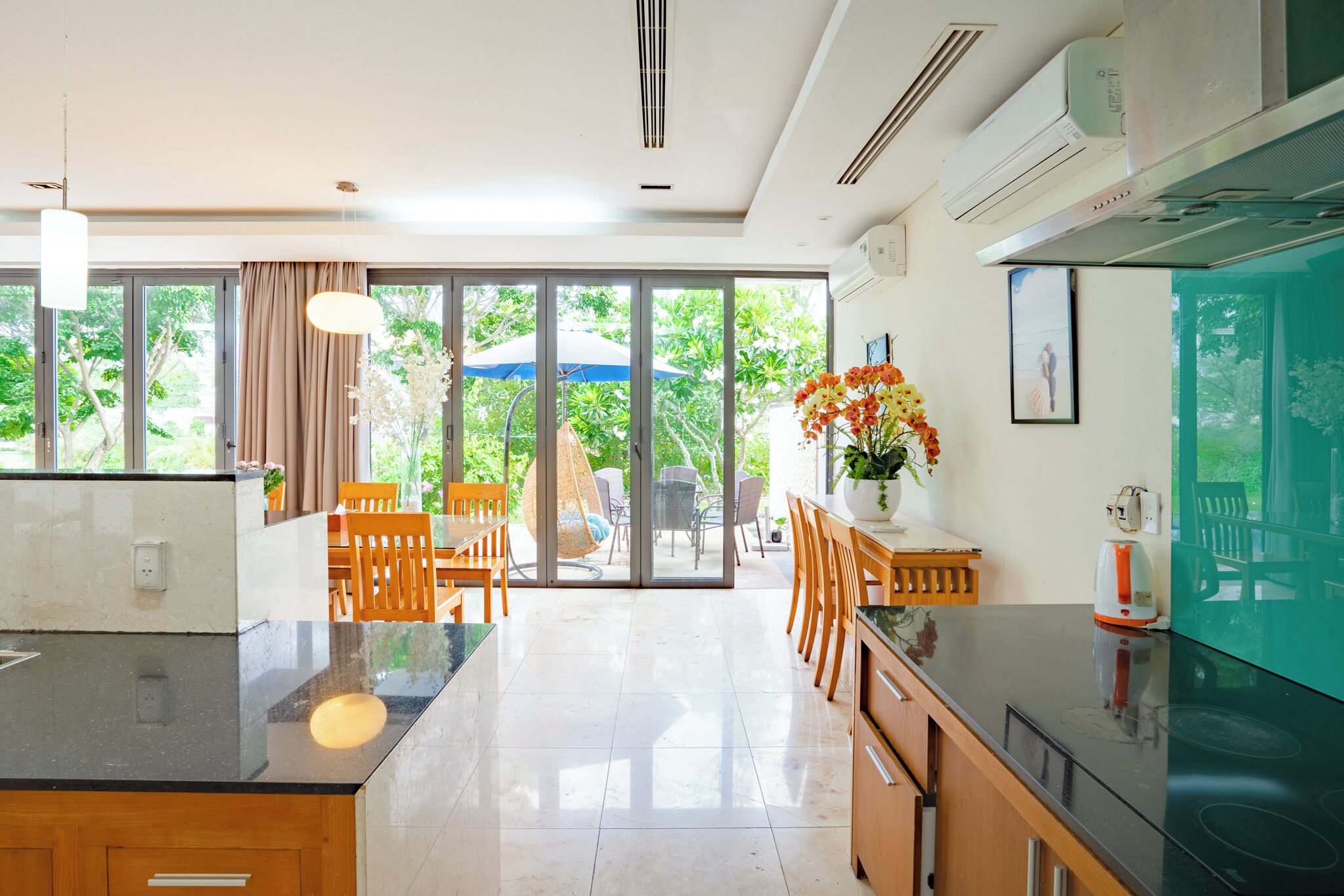 A modern kitchen with a large island, wooden cabinets, and a view through the glass doors to an outdoor patio area.