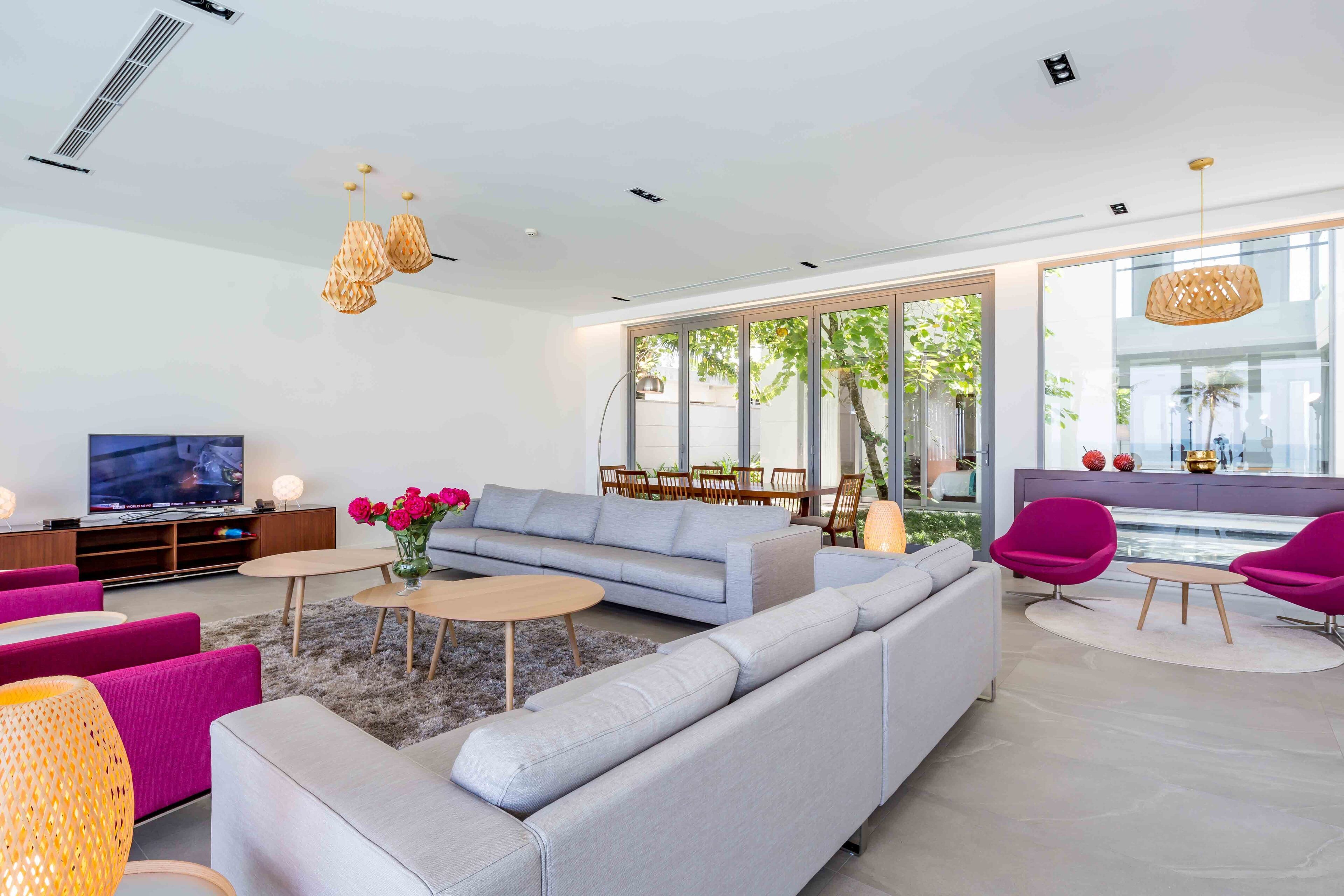 A modern living room with a grey sofa, pink chairs, and a TV on a wooden stand.