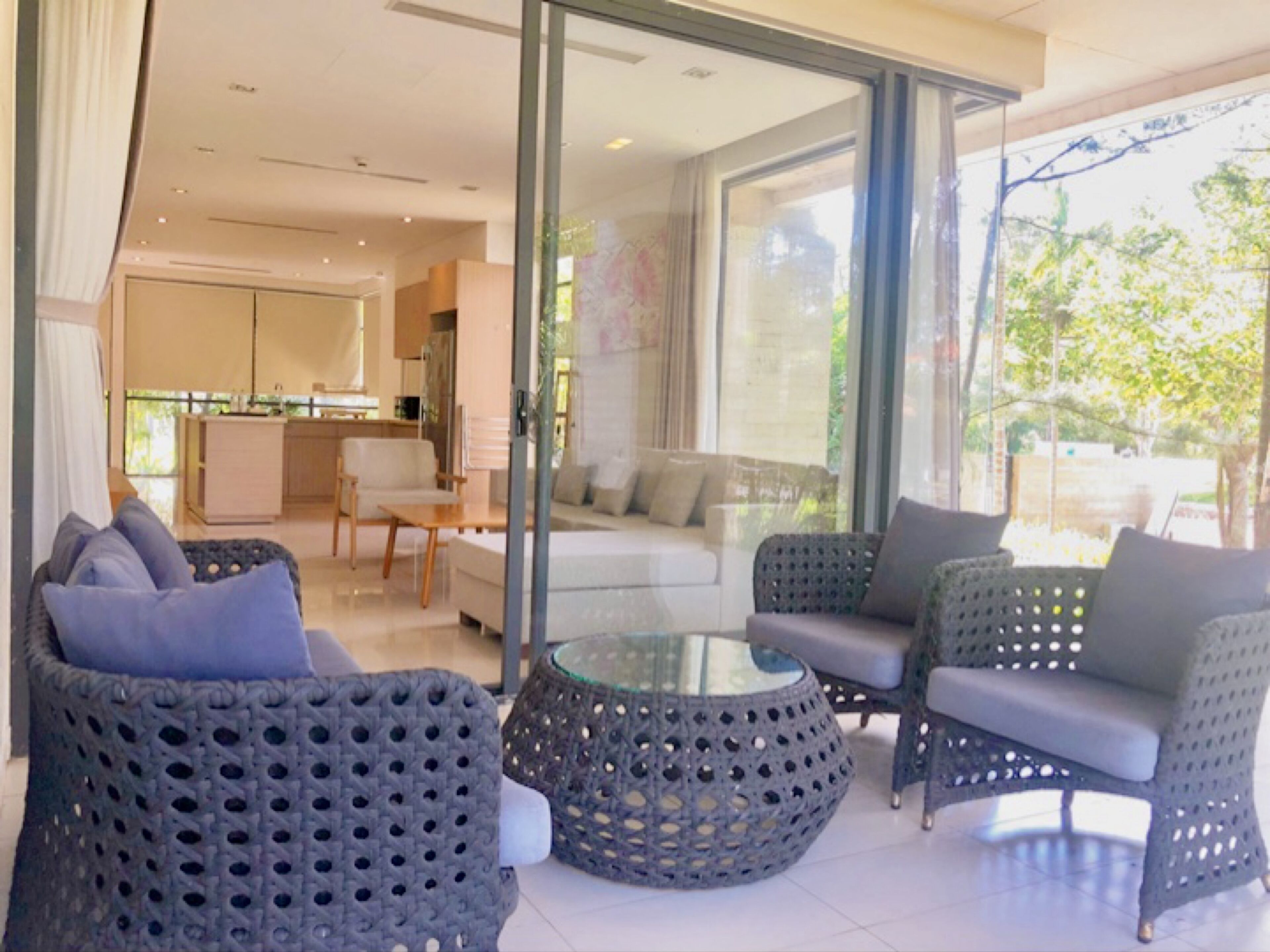 Una sala de estar moderna con muebles de mimbre, una mesa de centro de vidrio y vistas al exterior.