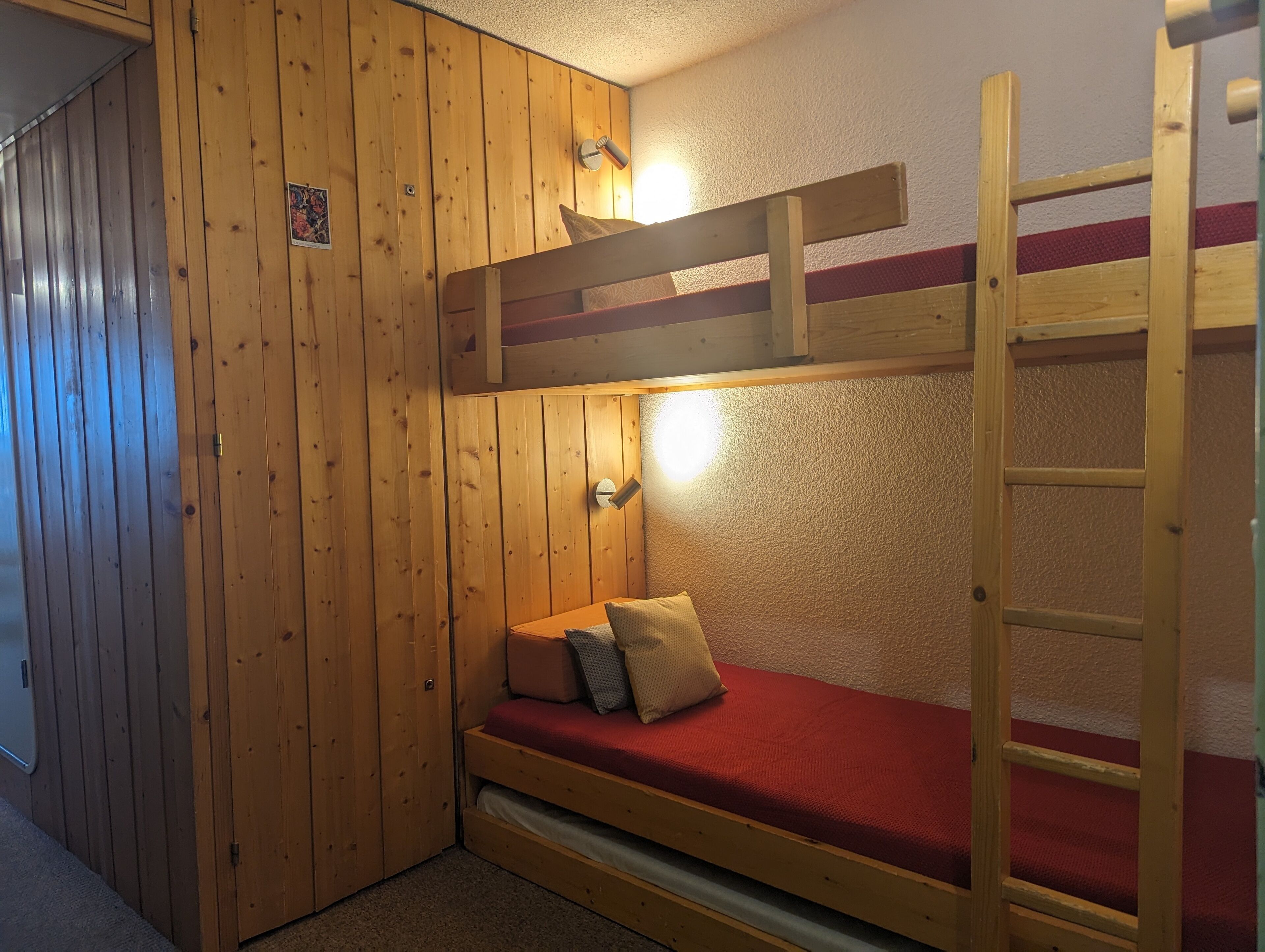A bunk bed room with wooden walls, a red mattress, and a ladder.