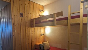 A bunk bed room with wooden walls, a red mattress, and a ladder.