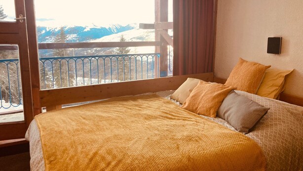 A bedroom with a bed, pillows, and a view of mountains through a balcony.