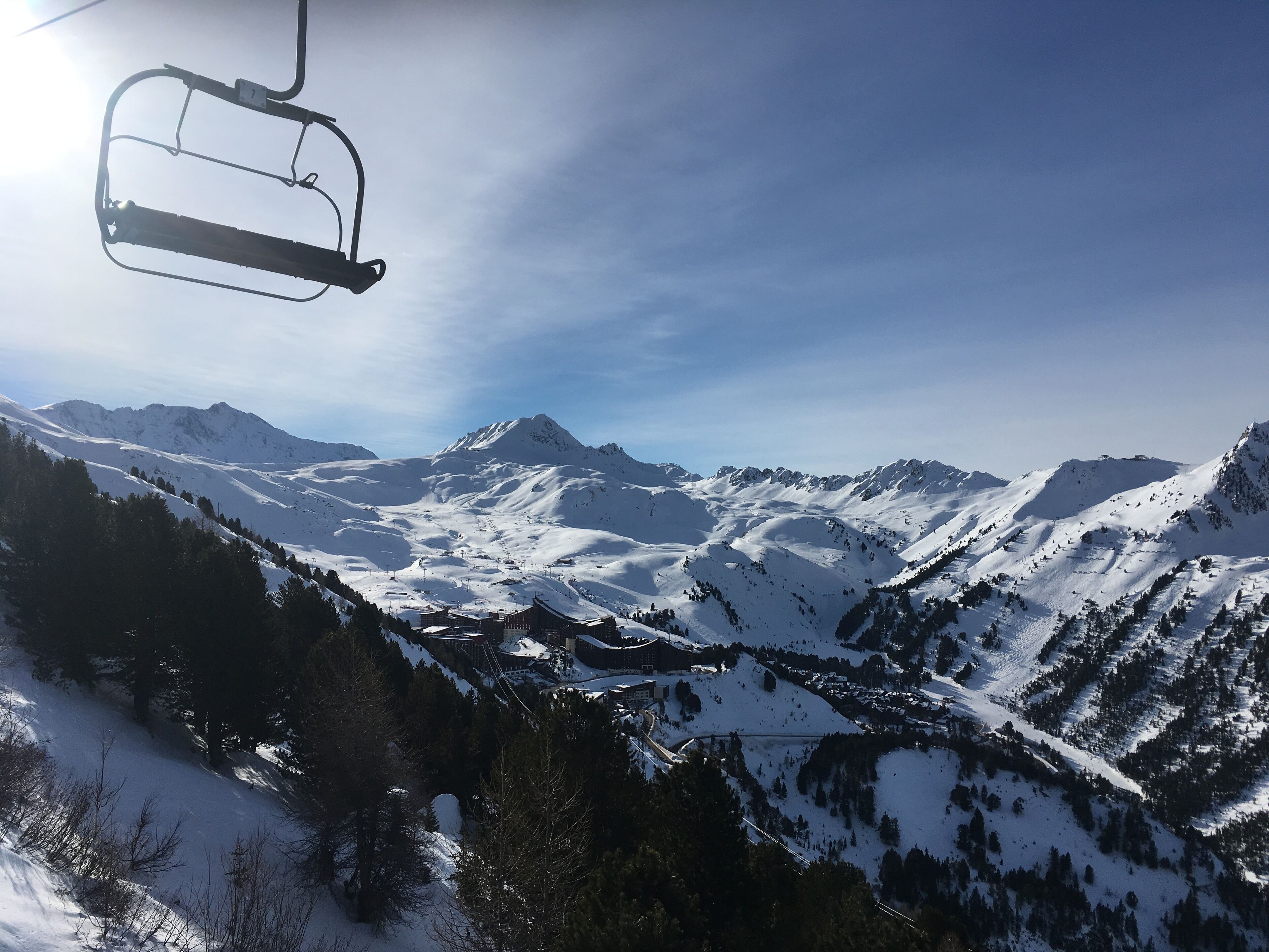 A ski lift chair suspended above a snowy mountain landscape with clear skies.
