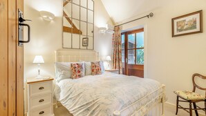 Ein Schlafzimmer mit Bett, Nachttischen, einem Sessel, einem Fenster mit Vorhängen, einem Spiegel und einem Bild an der Wand.