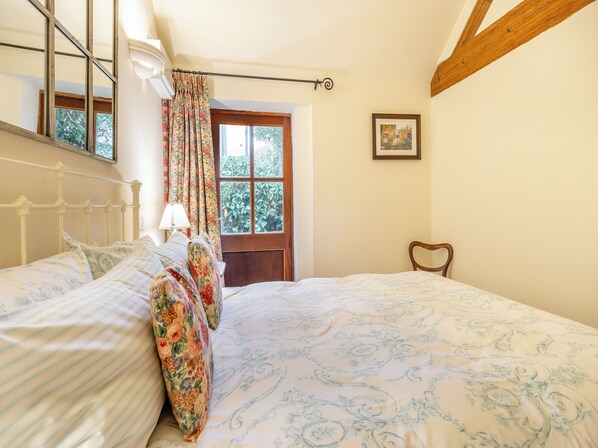 A bedroom with a bed, a window with curtains, a wooden chair, and a framed picture on the wall.