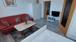 A room with a red sofa, a small table with a vase, a white wardrobe, a TV on a stand, and a door. - Ferienwohnung Modern (Burgstädt)