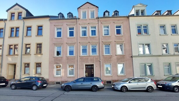 A row of three-story buildings with multiple windows and doors, parked cars in front, and a clear sky. - Ferienwohnung Modern (Burgstädt)