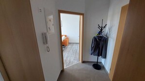 A narrow hallway with a door leading to a room with a bed and a small orange sofa. - Ferienwohnung Modern (Burgstädt)