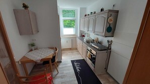 A compact kitchen with a dining area, a radiator, and a window with a view of greenery. - Ferienwohnung Modern (Burgstädt)