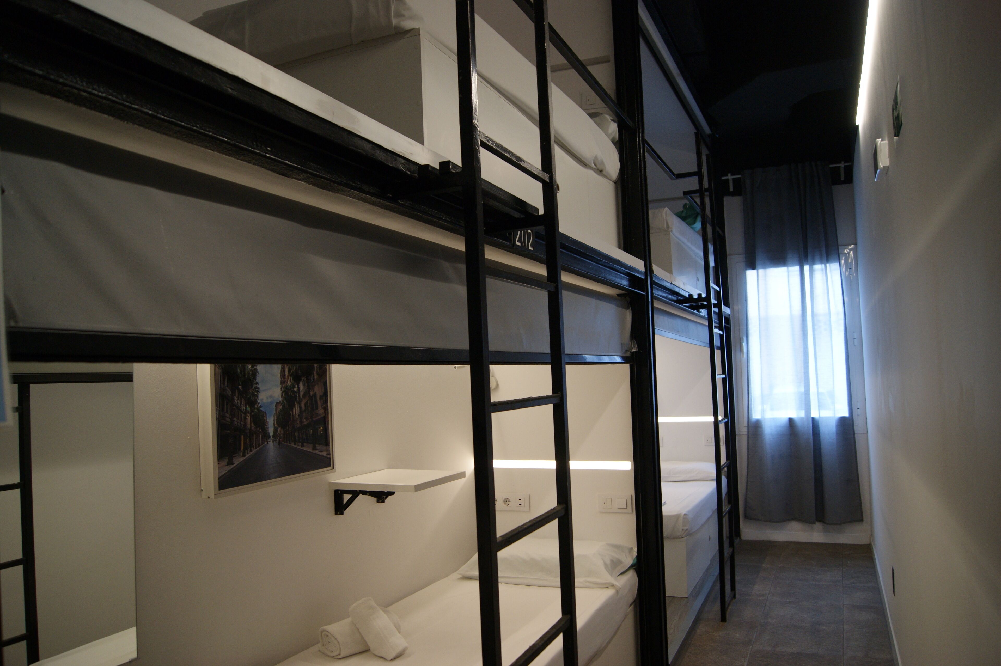 A bunk bed room with a shelf above the lower bunk and a window with curtains.