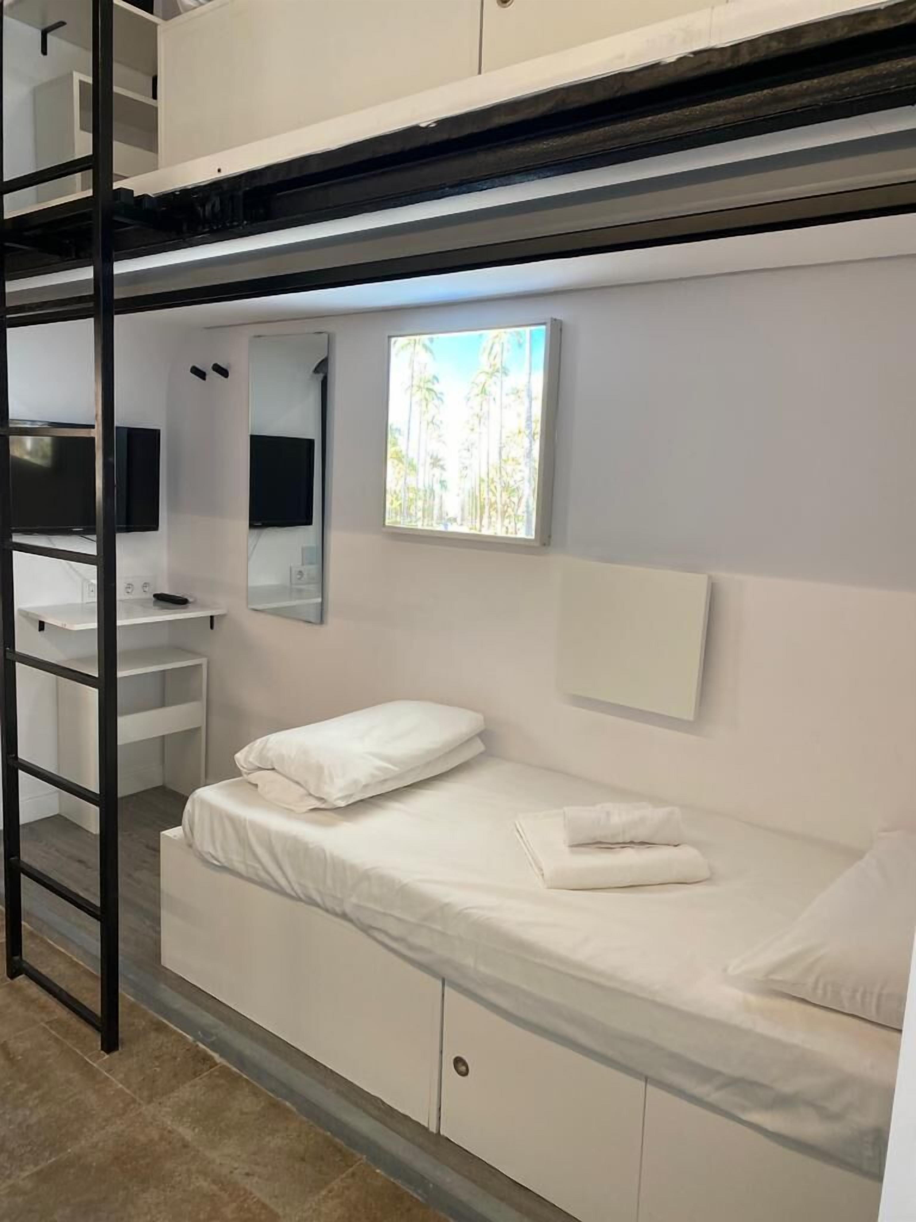A bunk bed room with a desk, mirror, and a window with a view of palm trees.