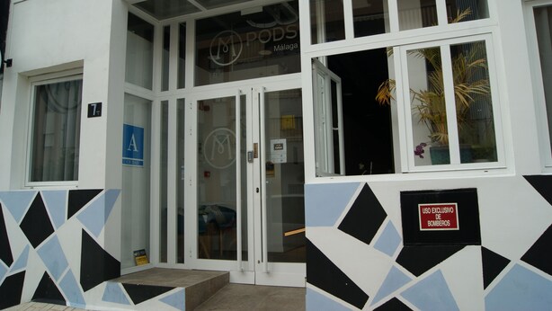 A building with a white facade, a glass door entrance, and a sign indicating 'PODS MALAGA'. - MPods Málaga (Málaga)