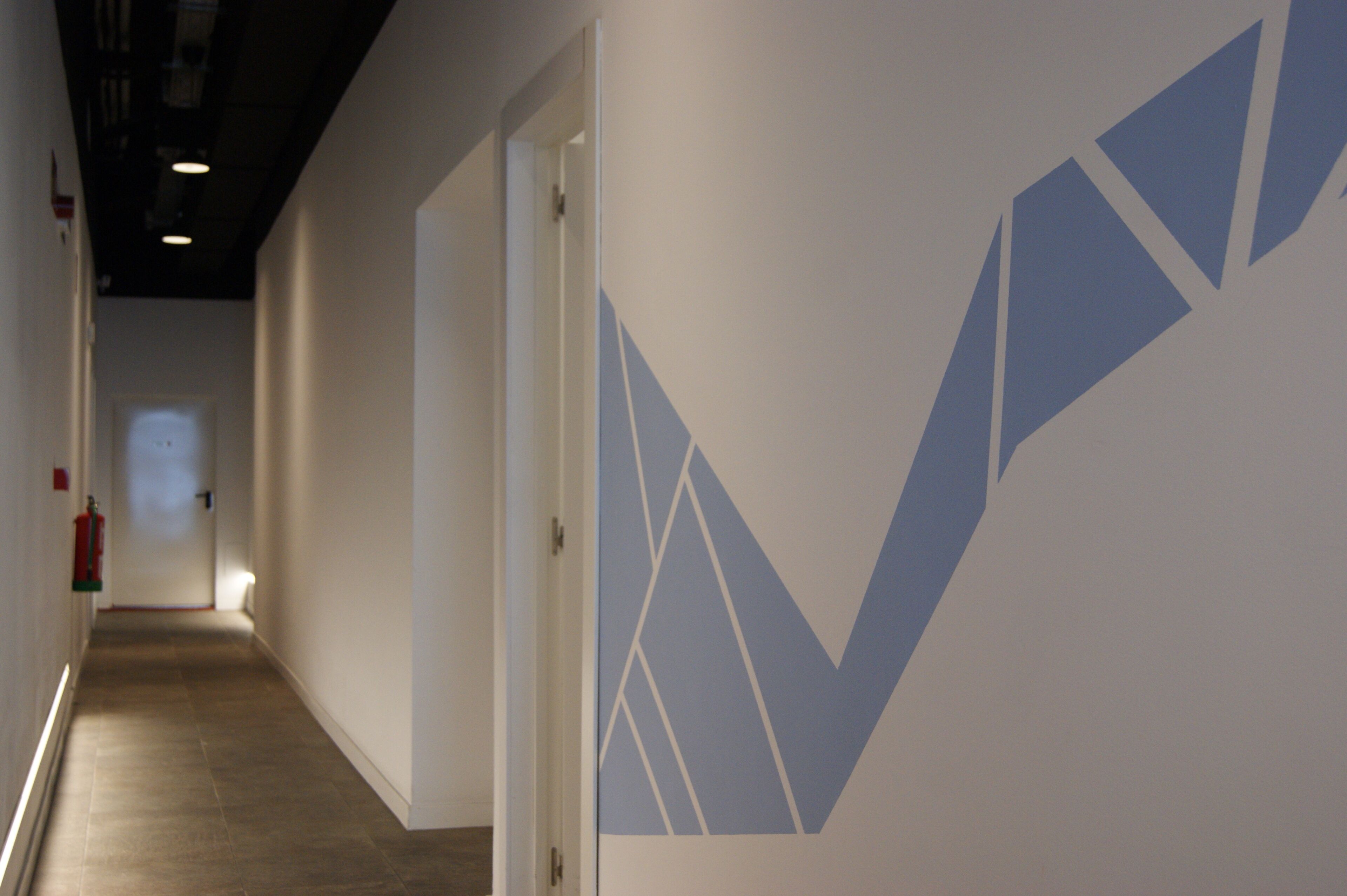 A hallway with a geometric wall design, a fire extinguisher, and a door at the end.