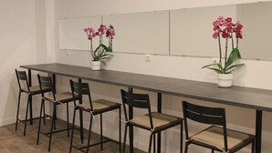 A long, narrow room with a dark wooden table and four chairs. There are two potted plants with pink flowers on the table. - MPods Málaga (Málaga)