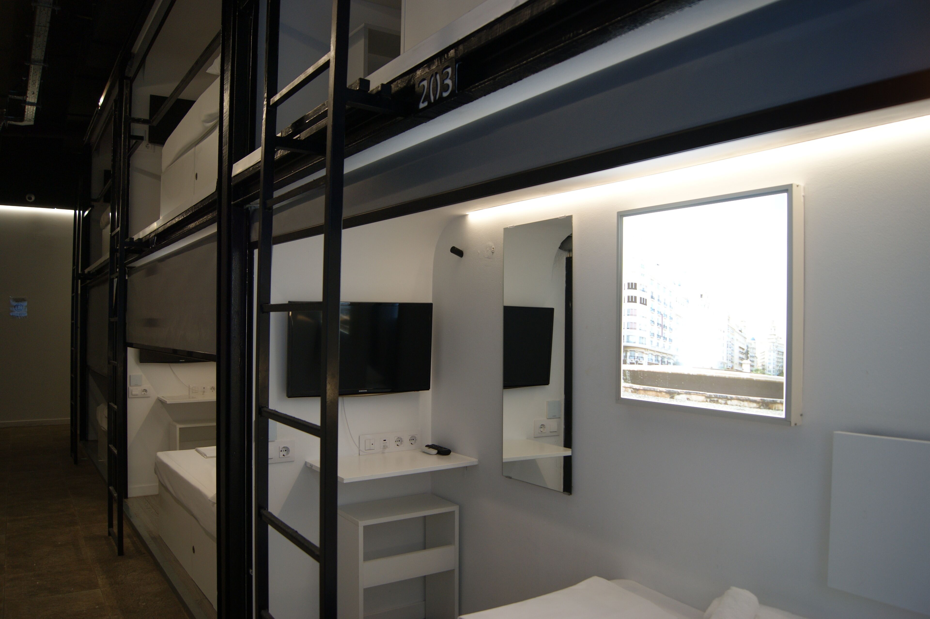 Una habitación de hotel moderna con literas, un televisor de pantalla plana, un ventanal con vistas a la ciudad y un diseño minimalista.