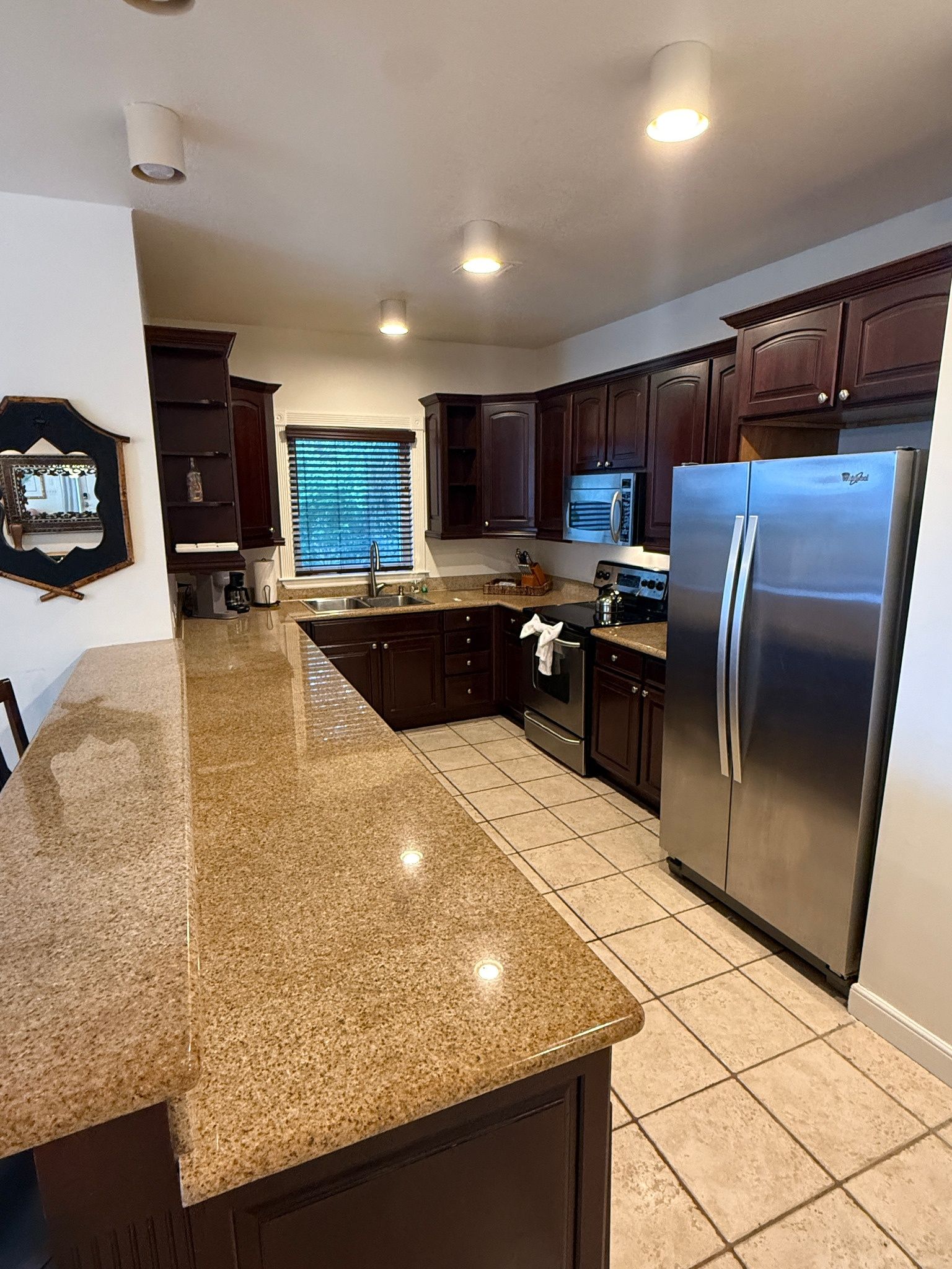 A modern kitchen with dark wood cabinets, a stainless steel refrigerator, and a granite countertop.