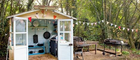 A rustic outdoor kitchen with a wooden deck, a table, and a grill.