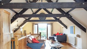 Ein großzügiges Loft mit freiliegenden Holzbalken, einer Holztreppe, einer Couch, einem Esstisch und Blick ins Freie.