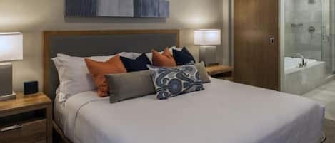 A modern hotel room with a large bed, a nightstand with a lamp, a wardrobe, and a shower area.