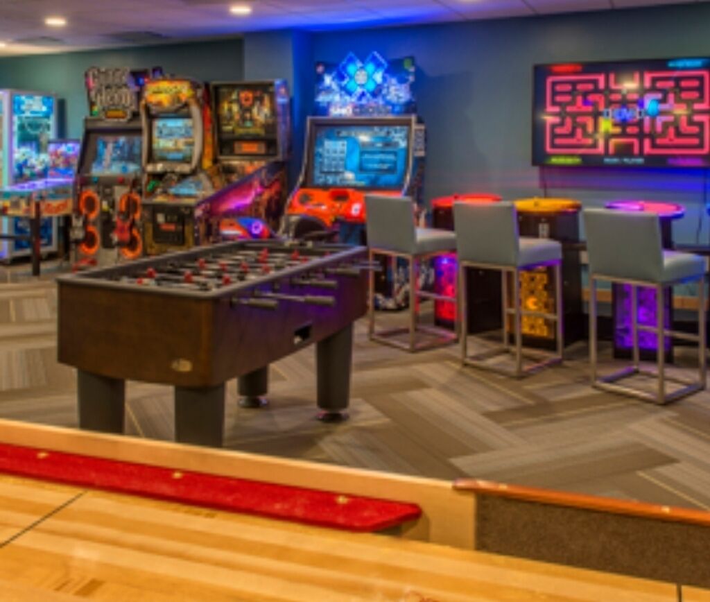 Un espace de jeux équipé de plusieurs bornes d’arcade, d’une table de baby-foot et de sièges de bar.