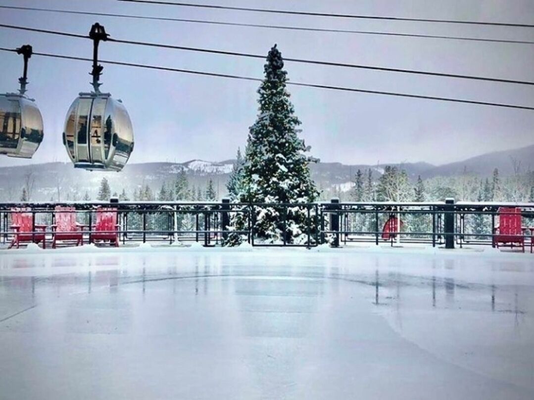 A snow-covered outdoor area with a large Christmas tree, a ski lift, and red chairs.