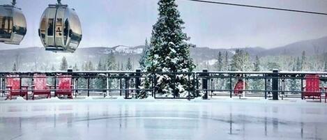 A snow-covered outdoor area with a large Christmas tree, a ski lift, and red chairs.