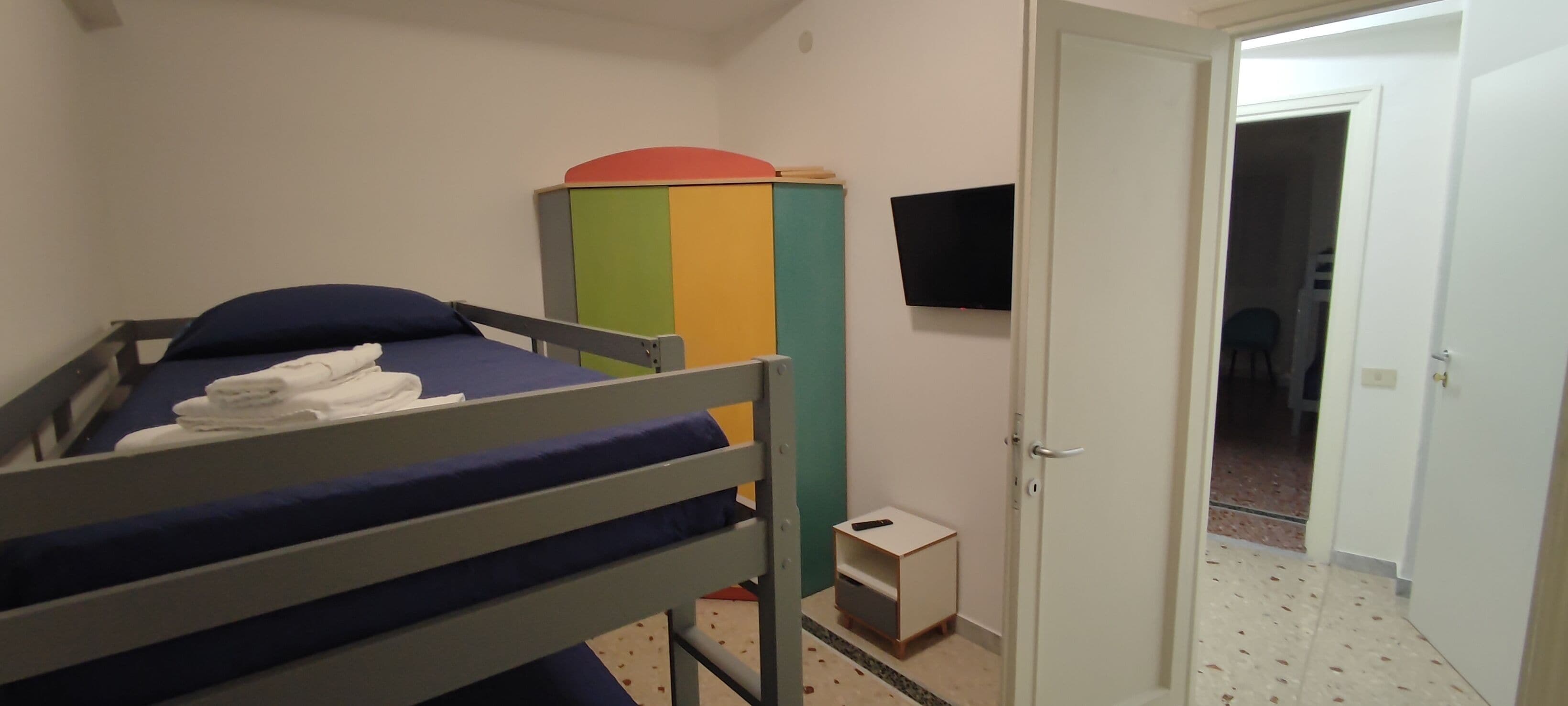 Un lit superposé avec un matelas bleu, une petite table de chevet et une armoire colorée.