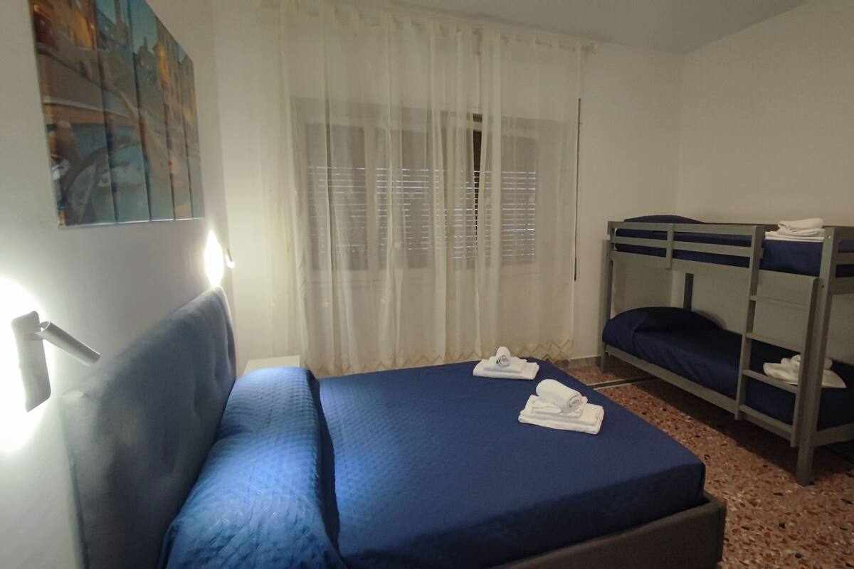 A room with a single bed, a bunk bed, a window with sheer curtains, and a painting on the wall.