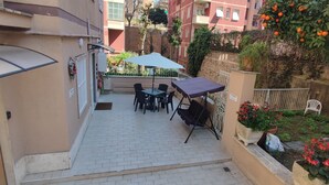 A small outdoor patio with a table and chairs, a covered seating area, and a view of a residential area with buildings and trees. - Vatican Green Garden (Rome)