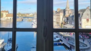 A view through a window with a grid pattern, displaying a harbor with boats, a river, and buildings with historical architecture.