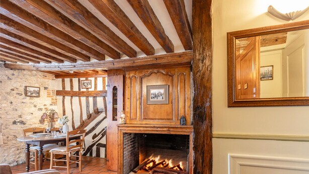 A rustic room with exposed wooden beams, a fireplace, stone walls, and a dining area with a table and chairs.