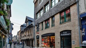 Una calle estrecha bordeada por edificios tradicionales europeos, incluyendo una tienda con un letrero que dice "Les Armateurs".