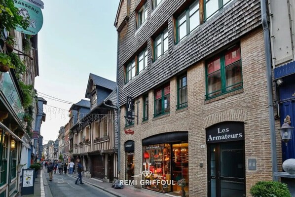 Una stretta via fiancheggiata da edifici europei tradizionali, tra cui un negozio con insegna 'Les Armateurs'.