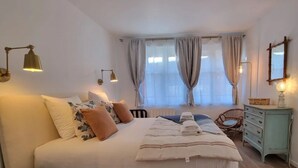 Un dormitorio con una cama grande, lámparas de noche, un aparador y una ventana con cortinas.