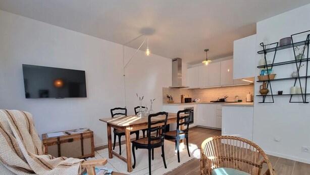 Una cocina moderna con gabinetes blancos, una mesa de comedor de madera y un televisor montado en la pared.