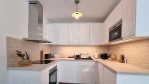 Una cocina moderna con armarios blancos, horno empotrado, microondas y fregadero.