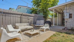 A backyard with a white outdoor seating area, including a sofa and two chairs, a small table, and a barbecue grill.