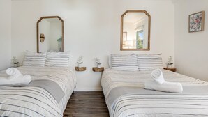 A hotel room with two beds, each with striped bedding and a mirror above. There are small wooden nightstands with potted orchids.