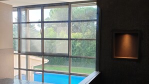 A modern bathroom with a large window, a bathtub, and a wall-mounted light fixture. - Luxury Villa in Costa Brava with Private Pool, Tennis Court, and Sauna
 (Pantans de Montbarbat)