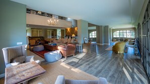 A spacious living room with a high ceiling, a chandelier, and a view of a kitchen and dining area. - Luxury Villa in Costa Brava with Private Pool, Tennis Court, and Sauna
 (Pantans de Montbarbat)