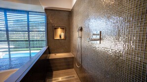 A modern bathroom with a glass shower enclosure, a built-in bench, and a view of the outdoors. - Luxury Villa in Costa Brava with Private Pool, Tennis Court, and Sauna
 (Pantans de Montbarbat)