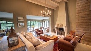 A spacious living room with a fireplace, leather sofas, a coffee table, and a chandelier. - Luxury Villa in Costa Brava with Private Pool, Tennis Court, and Sauna
 (Pantans de Montbarbat)